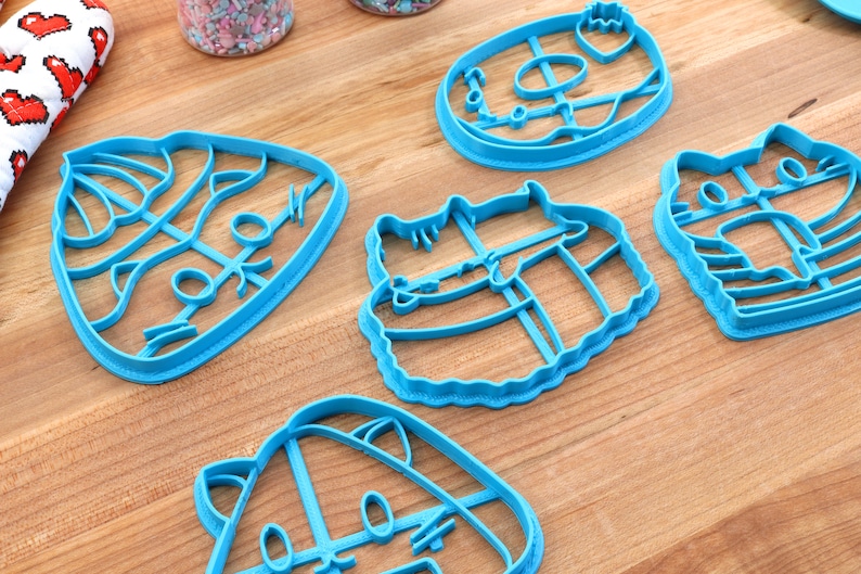 May include: Five blue plastic cookie cutters shaped like cats and a donut. The cutters are on a wooden surface.