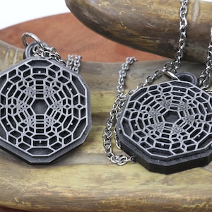 May include: Two silver necklaces with geometric pendant charms. The pendants are octagonal and feature a detailed, intricate design of a repeating pattern.