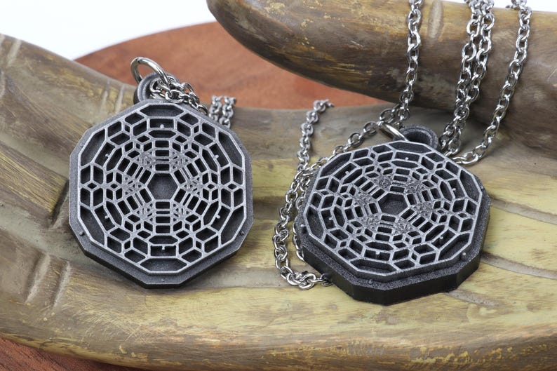 May include: Two silver necklaces with geometric pendant charms. The pendants are octagonal and feature a detailed, intricate design of a repeating pattern.