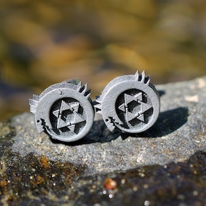 May include: Two silver cufflinks with a stylized star design. The star is made up of multiple triangles and is surrounded by a crescent moon shape.