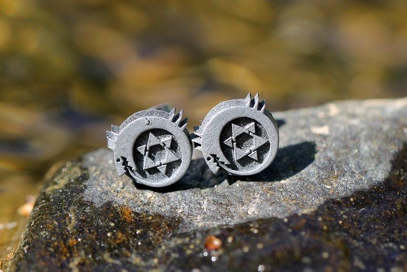 May include: Two silver cufflinks with a stylized star design. The star is made up of multiple triangles and is surrounded by a crescent moon shape.