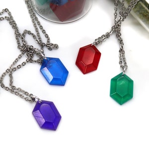 May include: Four necklaces with different colored gem pendants. The gems are red, blue, green, and purple. The necklaces are silver chains.