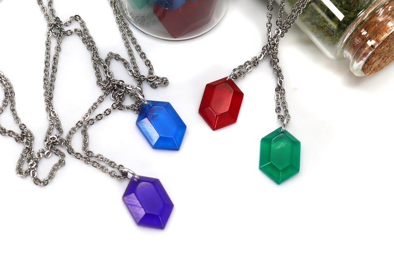 May include: Four necklaces with different colored gem pendants. The gems are red, blue, green, and purple. The necklaces are silver chains.