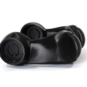 May include: A pair of black plastic knobs with a circular design on the top. The knobs are connected by a smooth, curved piece.