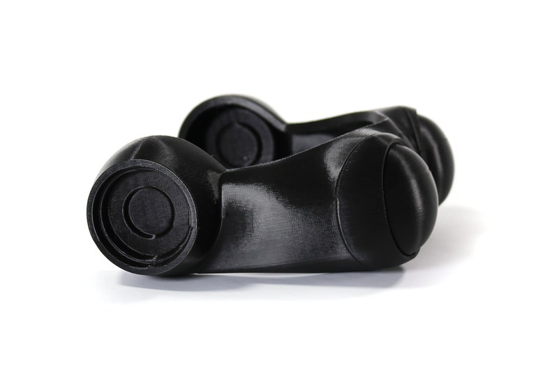 May include: A pair of black plastic knobs with a circular design on the top. The knobs are connected by a smooth, curved piece.
