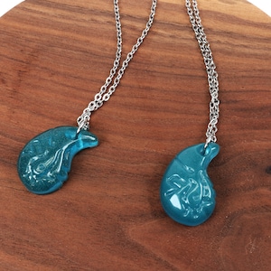 May include: Two silver necklaces with teal blue pendant charms shaped like a teardrop. The charms have a detailed design.