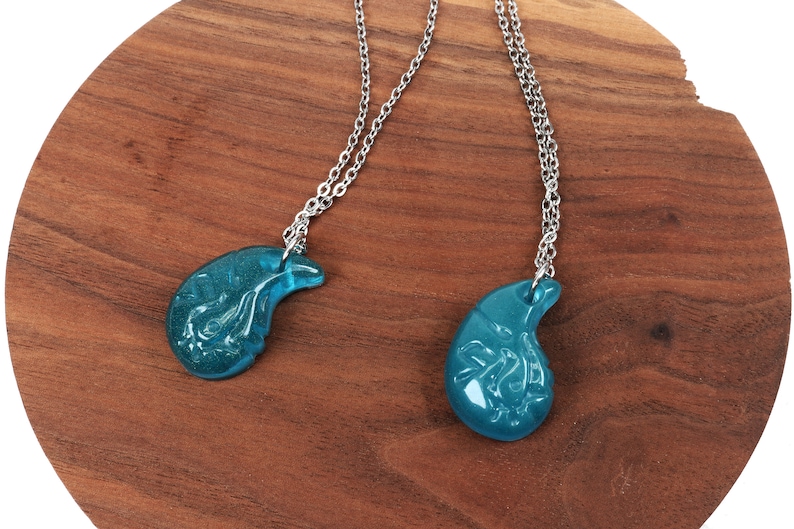 May include: Two silver necklaces with teal blue pendant charms shaped like a teardrop. The charms have a detailed design.