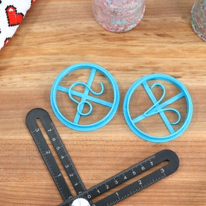 May include: Two blue plastic cookie cutters shaped like the letter "S" with a decorative flourish. The cutters are on a wooden surface.