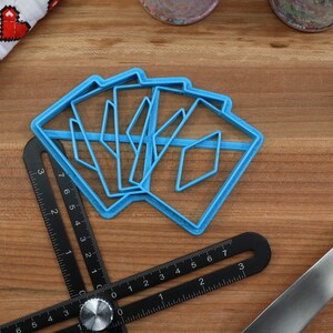 May include: A set of five blue plastic cookie cutters shaped like diamonds, arranged on a wooden surface. The cutters are stacked on top of each other, with the largest cutter on the bottom and the smallest cutter on top.