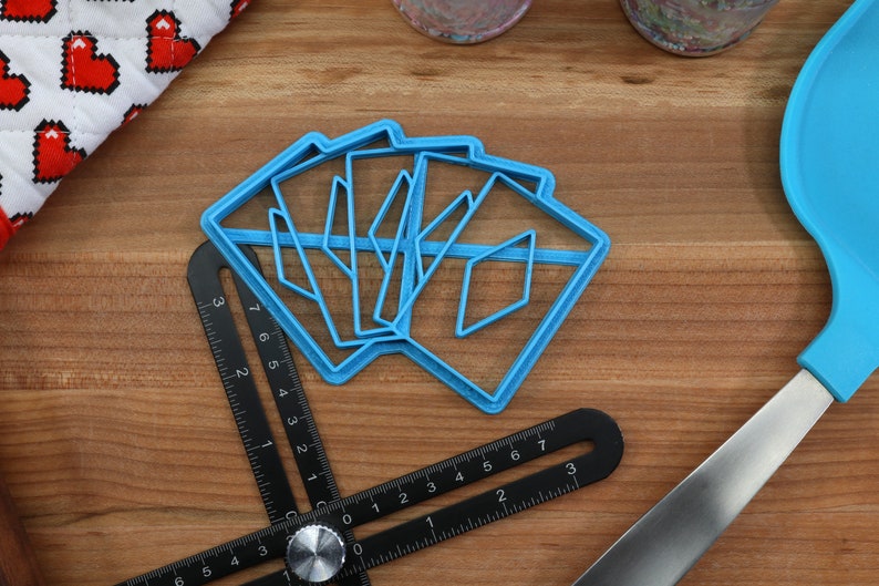 May include: A set of five blue plastic cookie cutters shaped like diamonds, arranged on a wooden surface. The cutters are stacked on top of each other, with the largest cutter on the bottom and the smallest cutter on top.
