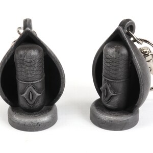 May include: Two silver-colored microphone keychain charms. Each charm features a microphone with a detailed design and a small eye symbol. One charm has a silver-colored ring attached for attaching to a keychain.