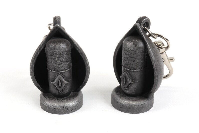 May include: Two silver-colored microphone keychain charms. Each charm features a microphone with a detailed design and a small eye symbol. One charm has a silver-colored ring attached for attaching to a keychain.