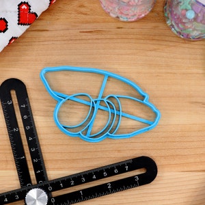 May include: Blue plastic cookie cutter shaped like a stack of three bagels. The cutter is on a wooden surface.