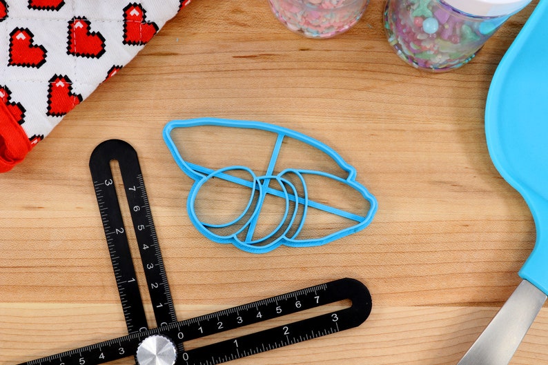May include: Blue plastic cookie cutter shaped like a stack of three bagels. The cutter is on a wooden surface.