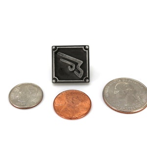 May include: A silver metal pin with a black square background and a silver stylized wing design. The pin is surrounded by three US coins: a quarter, a dime, and a penny.