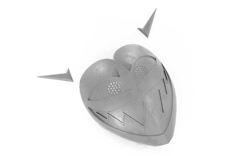 May include: A silver heart-shaped mask with a toothy grin, two eyes, and two small points on top.