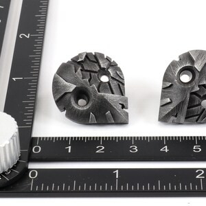 May include: Two silver metal decorative pieces with a textured, geometric design. Each piece has two holes.