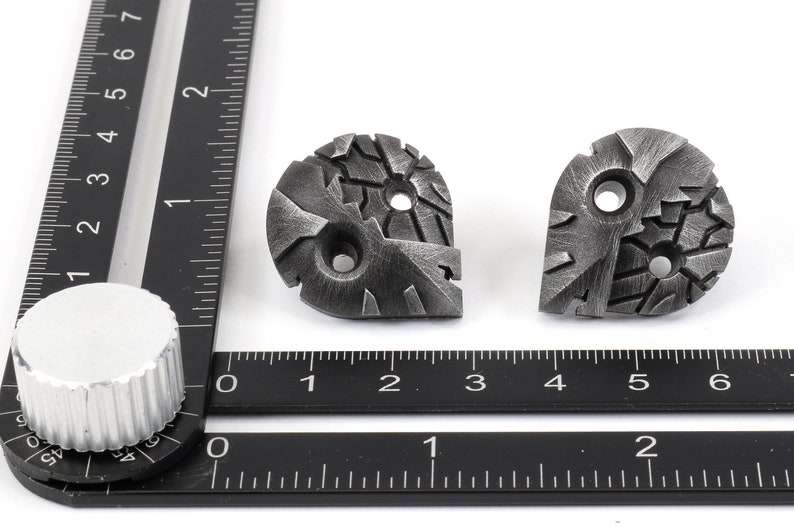 May include: Two silver metal decorative pieces with a textured, geometric design. Each piece has two holes.