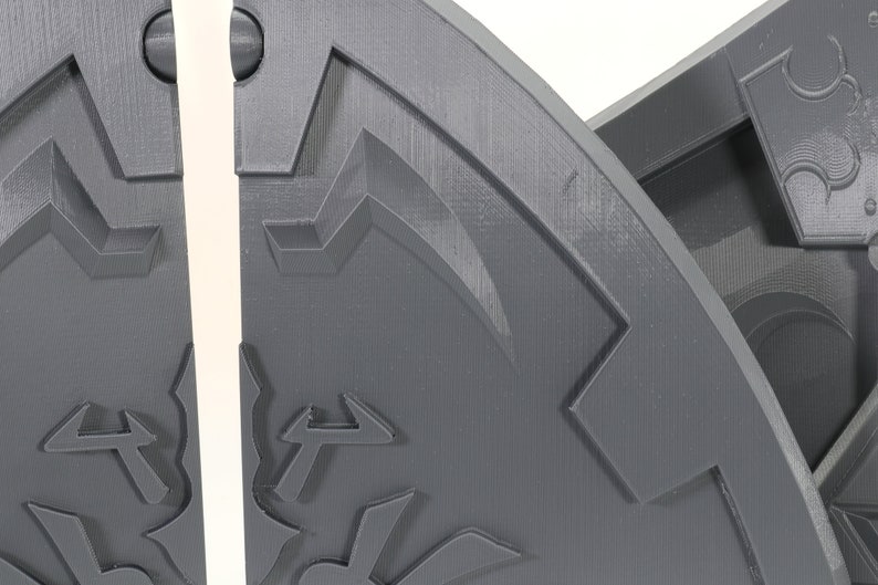 May include: Close-up of a gray, 3D printed, segmented, circular object with a textured surface and a geometric design. The object is split into two sections.