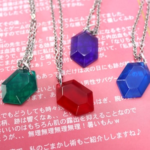 May include: Four necklaces with different colored gem-shaped pendants. The pendants are red, blue, green, and purple. The necklaces are silver chains.