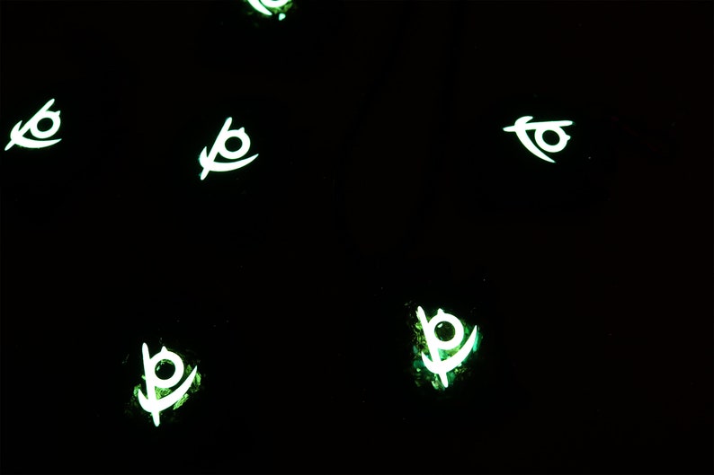 May include: Five glowing green and white symbols on a black background. The symbols are stylized eyes with a curved line extending from the bottom.