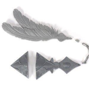 May include: A gray plastic feather and a gray plastic chain with a triangular pendant. The pendant has a geometric design.