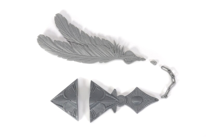 May include: A gray plastic feather and a gray plastic chain with a triangular pendant. The pendant has a geometric design.