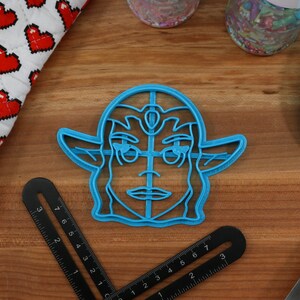 May include: Blue plastic cookie cutter shaped like a cartoon character with a crown and pointed ears. The character has a detailed face with a large nose and eyes.