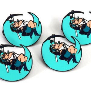 May include: Four teal blue and black enamel pins featuring a cartoon character with long teal blue hair sitting on a crescent moon. The character is holding a black scythe.