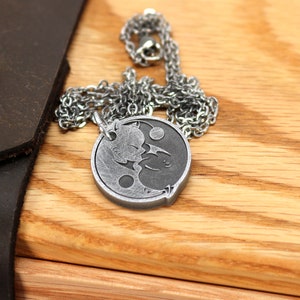 May include: A silver necklace with a yin yang pendant featuring two cats facing each other. The pendant is on a wooden surface.