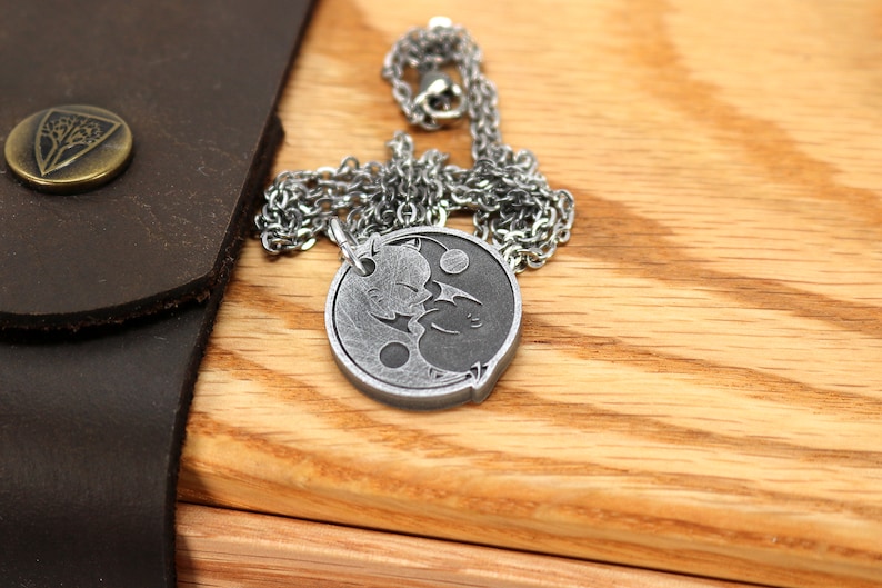 May include: A silver necklace with a yin yang pendant featuring two cats facing each other. The pendant is on a wooden surface.