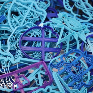Op de afbeelding: Een verzameling blauwe en paarse plastic koekjesvormen in verschillende vormen, waaronder een hart, een ster en een cirkel.