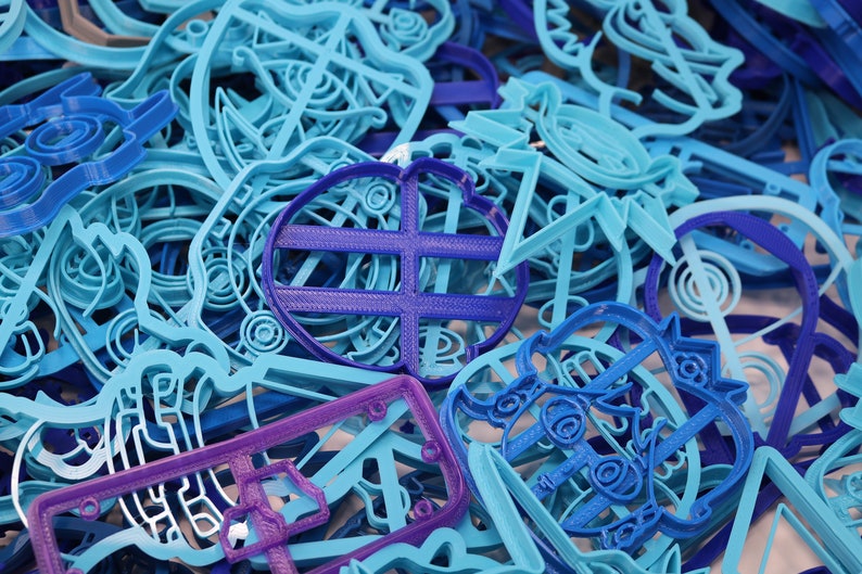 Op de afbeelding: Een verzameling blauwe en paarse plastic koekjesvormen in verschillende vormen, waaronder een hart, een ster en een cirkel.