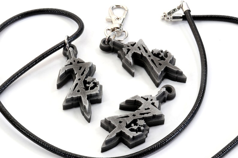 May include: Three silver-colored pendants with a stylized design, one on a black cord necklace, one on a silver chain, and one loose. The pendants feature a geometric design with a sword-like shape.