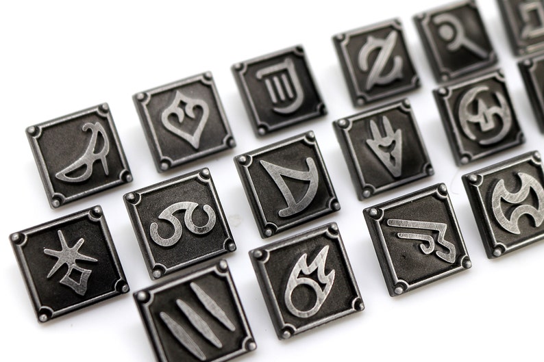 May include: A set of 16 silver-toned metal pins with different symbols. Each pin is square-shaped and has a raised design. The symbols include a musical note, a heart, a star, a crescent moon, a sword, a flame, and more.