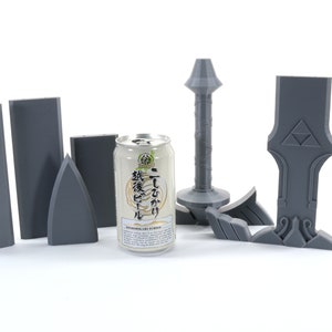 Puede incluir: Un conjunto de piezas de pl&aacute;stico gris para construir un modelo de espada. Las piezas incluyen la hoja, la empu&ntilde;adura y la guarda. Una lata de cerveza japonesa se encuentra en el centro de la imagen.