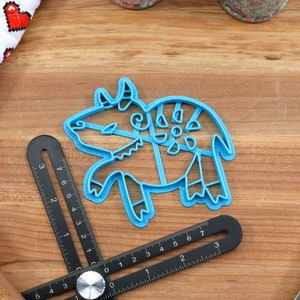 May include: Blue plastic cookie cutter shaped like a stylized bull with intricate details. The cutter is on a wooden surface.