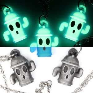 May include: Three silver-colored necklaces with glow-in-the-dark pendants shaped like a fire hydrant with a face. The pendants are on a black background and glow green.