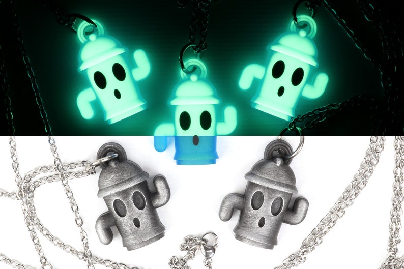May include: Three silver-colored necklaces with glow-in-the-dark pendants shaped like a fire hydrant with a face. The pendants are on a black background and glow green.