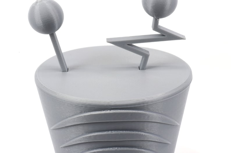Pode incluir: Um modelo 3D impresso em cinza de um personagem de desenho animado estilizado com duas cabe&ccedil;as redondas e um bra&ccedil;o em forma de ziguezague.