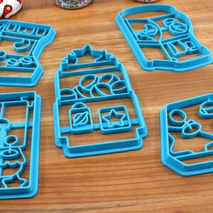 May include: Five blue plastic cookie cutters shaped like different vending machines. The cutters are on a wooden surface.