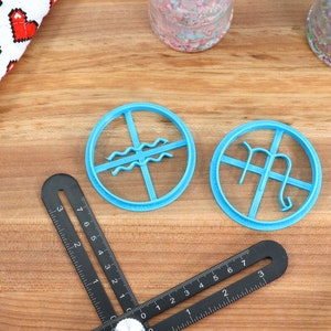 May include: Two blue plastic cookie cutters shaped like astrological signs. The cutter on the left is Aquarius and the cutter on the right is Virgo.