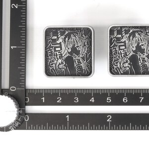 Puede incluir: Dos pines de metal de color plateado con una imagen en blanco y negro de un personaje de anime. Los pines presentan texto japon&eacute;s y tienen un di&aacute;metro de aproximadamente 2,5 cm.