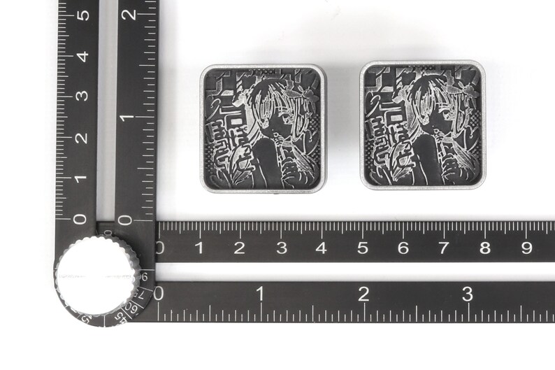 Puede incluir: Dos pines de metal de color plateado con una imagen en blanco y negro de un personaje de anime. Los pines presentan texto japon&eacute;s y tienen un di&aacute;metro de aproximadamente 2,5 cm.