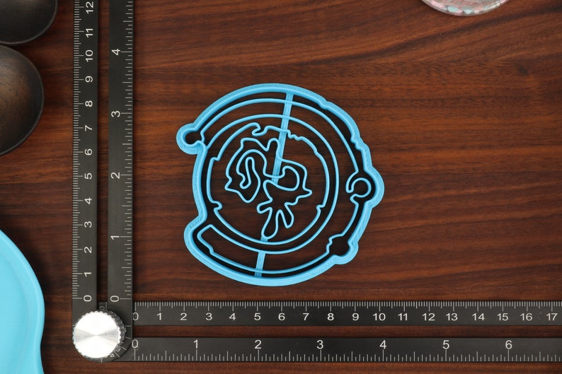 Puede incluir: Un cortador de galletas de pl&aacute;stico azul en forma de c&iacute;rculo con un dise&ntilde;o en el interior. El dise&ntilde;o es una imagen estilizada de un planeta con un anillo alrededor.