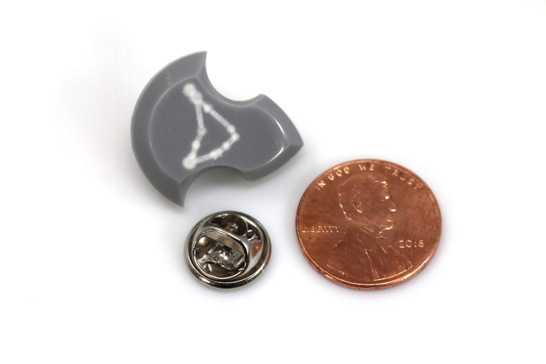 Puede incluir: Un pin de esmalte gris con un contorno blanco de la constelaci&oacute;n de Acuario. El pin es aproximadamente del tama&ntilde;o de una moneda de un centavo de d&oacute;lar estadounidense.