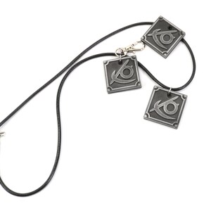 May include: A black leather necklace with three silver pendants featuring a stylized eye design.