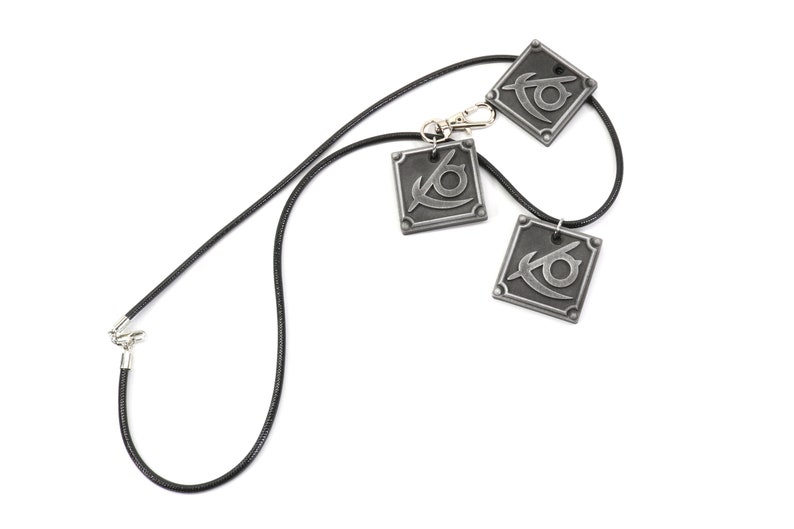 May include: A black leather necklace with three silver pendants featuring a stylized eye design.