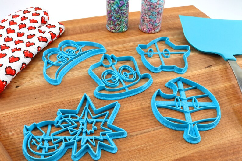 May include: A set of six blue plastic cookie cutters shaped like video game characters. The cutters are on a wooden surface.