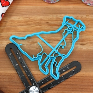 May include: A blue plastic cookie cutter shaped like a goat. The cutter is on a wooden surface with a ruler.